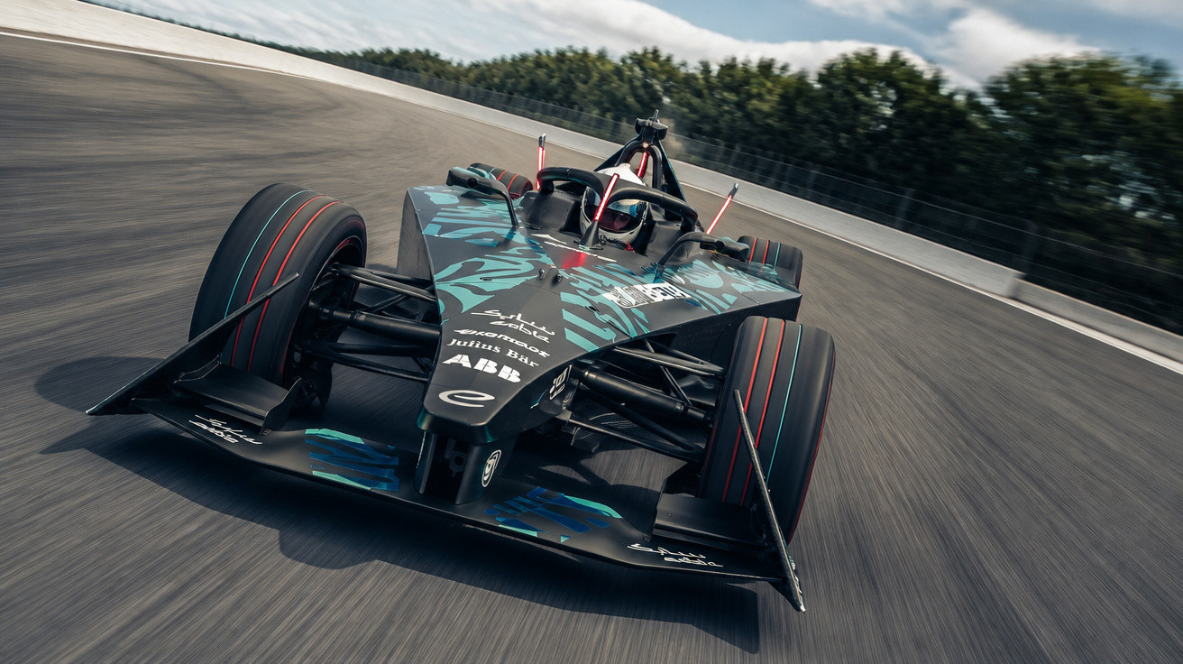 Carro de Fórmula E em alta velocidade em curva de autódromo sob céu nublado.