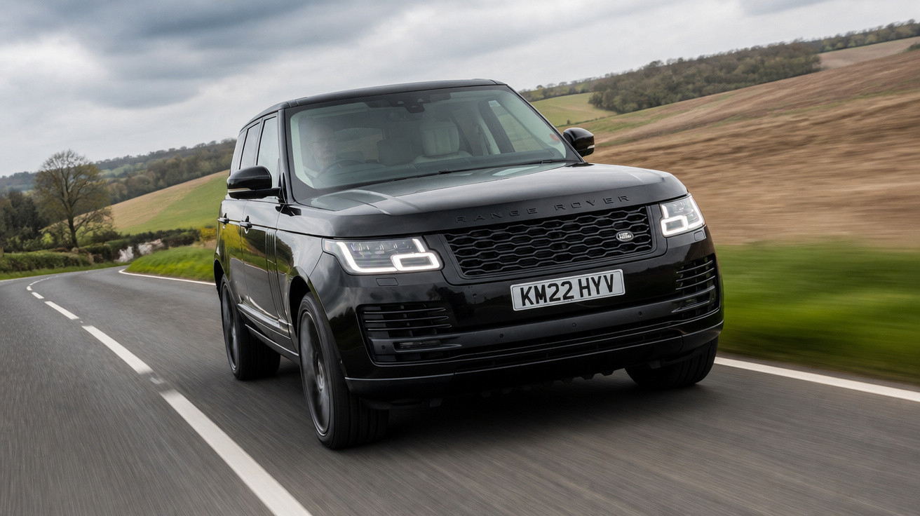 Carro SUV preto Range Rover trafegando em estrada asfaltada com paisagem rural ao fundo.