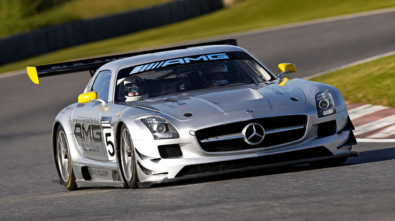 Carro de corrida Mercedes-AMG prata com detalhes amarelos em pista de corrida asfaltada.