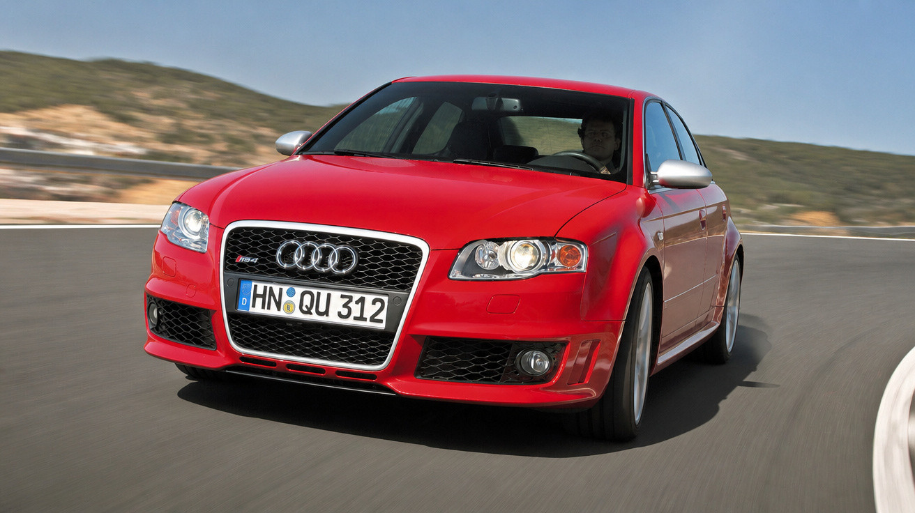 Carro esportivo Audi vermelho em curva de estrada asfaltada com fundo de montanhas.