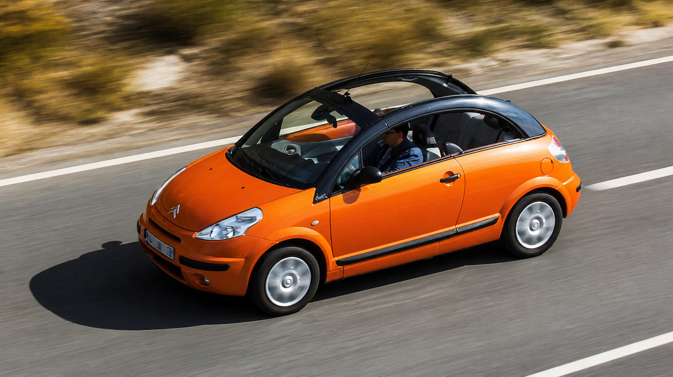 Carro compacto laranja com teto solar aberto, em movimento numa estrada asfaltada.