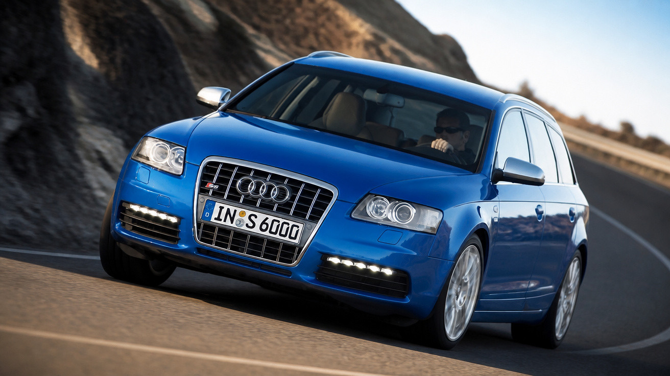 Carro azul Audi S6 Avant em curva numa estrada de montanha, com motorista usando óculos escuros.