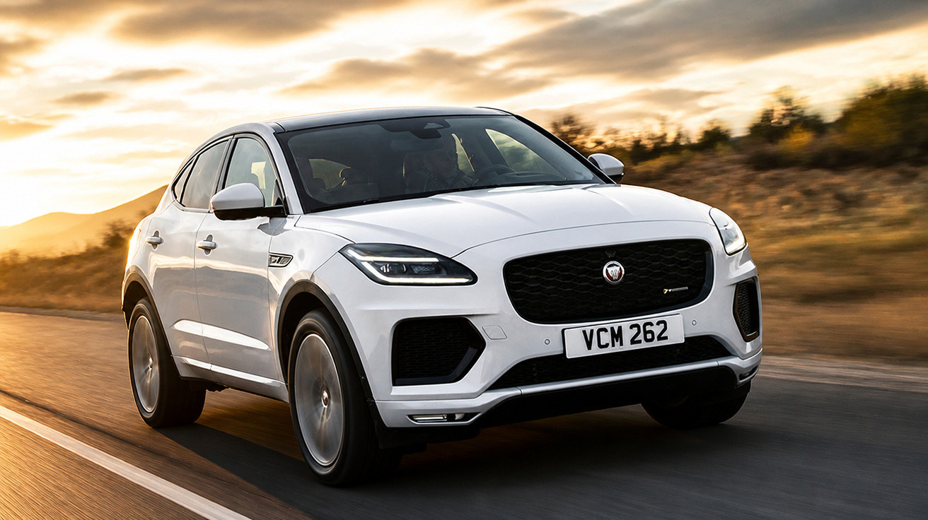 Carro SUV branco Jaguar E-Pace em estrada durante pôr do sol com céu dourado e colinas ao fundo.