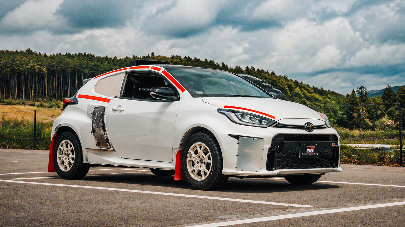 Carro esporte branco com detalhes vermelhos e rodas brancas estacionado em área aberta com árvores ao fundo.