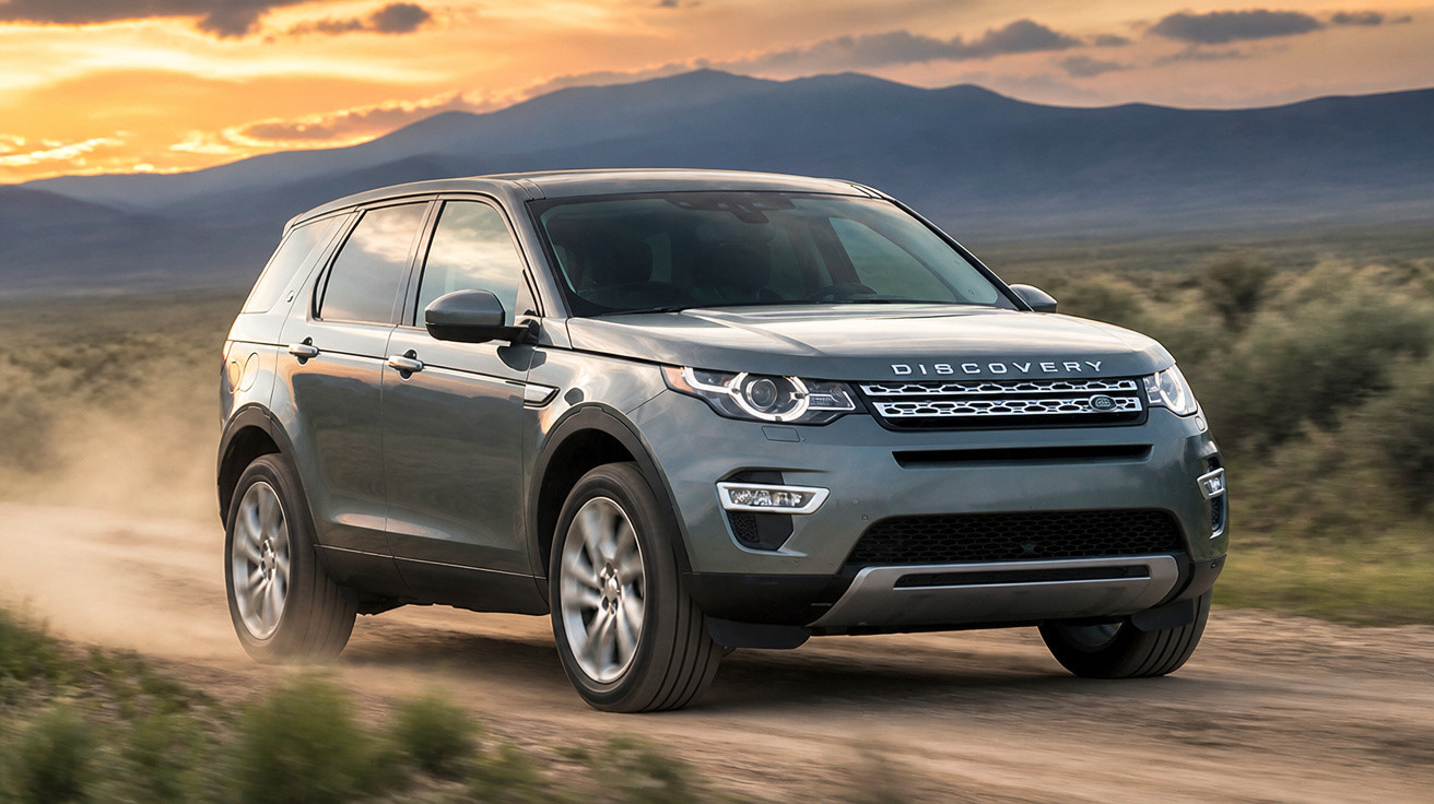 SUV Land Rover Discovery cinza trafegando em estrada de terra ao pôr do sol com montanhas ao fundo