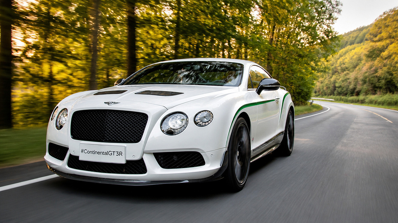 Carro esportivo branco Bentley Continental GT3R em estrada sinuosa cercada por árvores.